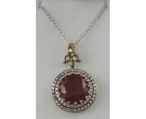 A ruby and cubic zirconia pendant, the circular claw set central stone within two bands and a gem set bail on a fine chain.