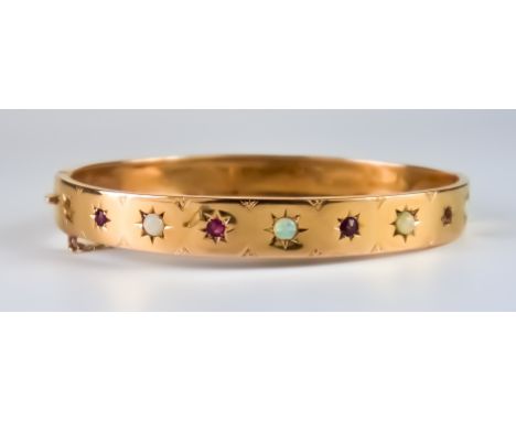 An Early 20th Century Gem Set Bangle, 9ct gold set with small red stones and small opals, 185mm circumference, gross weight 9
