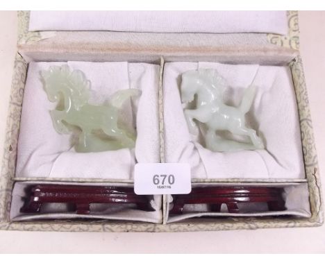 A pair of carved 'jade' horses on wooden stands, boxed.