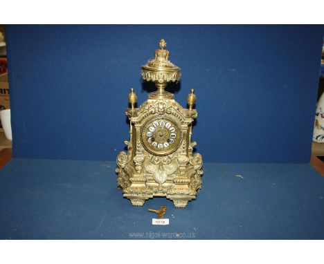 An ornate brass Mantle clock in Baroque style having swags and pillars and urn finial to the top, white enamel Roman numerals