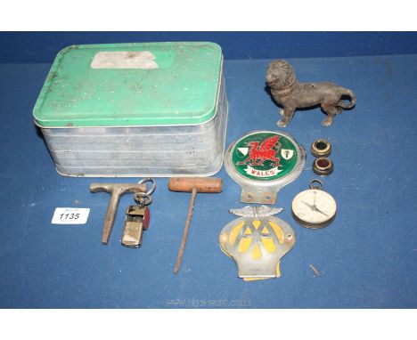 An aluminium tin and contents including AA badge, Wales enamel car badge, compass, brass lion, Acme whistle, etc.