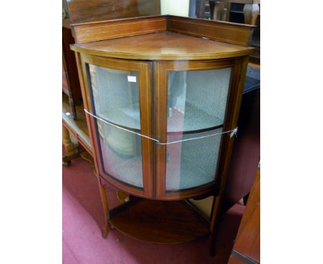 An Edwardian mahogany and satinwood strung double door glazed bow front corner cabinet, having platform undertier