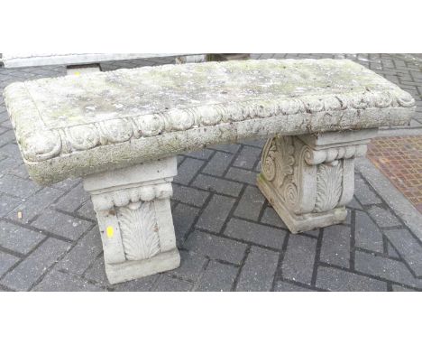 A reconstituted stone garden two-seater slightly curved bench seat, raised on floral scroll pedestal end supports, length 104