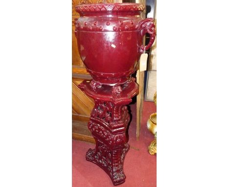 A large red glazed pottery twin handled urn on stand of slender bulbous form, with elephant head and trunk handles, raised on