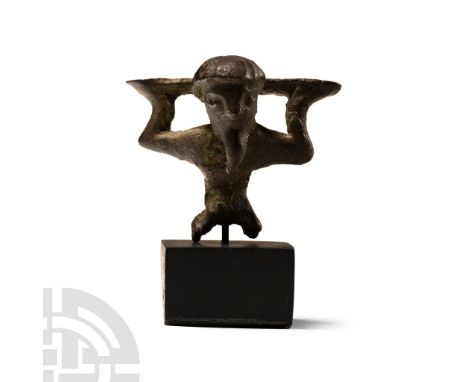 Circa 4th century B.C.. Appliqué formed as a kneeling male with arms bent supporting a shelf above the shoulders; the hair cu