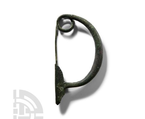 8th-6th century B.C.. Single-piece fibula comprising a thick bow with integral coiled spring to one end developing to a sturd