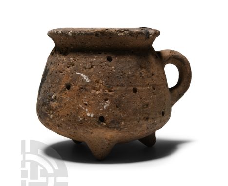 Early Bronze Age, 2700-2000 B.C.. Squat cup with broad rim and three stub feet, loop handle; pierced in several places.  209 