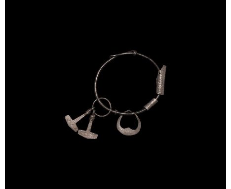 9th-12th century AD. A silver round-section bracelet with sliding closure, amuletic charms comprising two rolled silver dirhe