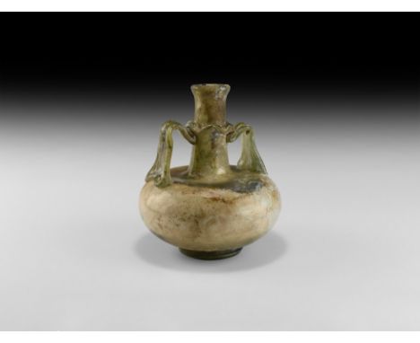 1st-3rd century AD. A green glass squat jar with tapering neck and chamfered rim, wavy applied collar and two similar strap h