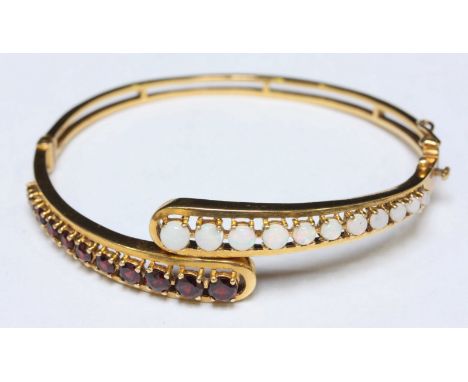 A 9ct gold and garnet stiff bangle, each teardrop end decorated with a graduated row of stones. 15.5 grams.