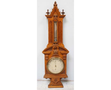A Victorian Gothic style carved oak Aneroid barometer, the circular barometer dial with engraved decoration, thermometer abov
