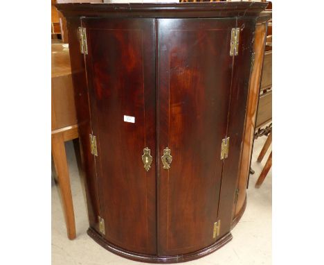 A Georgian mahogany bow front corner cupboard enclosed by 2 crossbanded doors