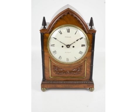 An early 19th century mahogany bracket clock with arched top, cone finials, reeded pilasters, and foliate carved panel to pat