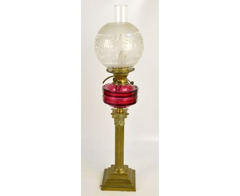 An early 20th century brass oil lamp modelled as a Corinthian column, with ruby glass reservoir and a globular floral decorat