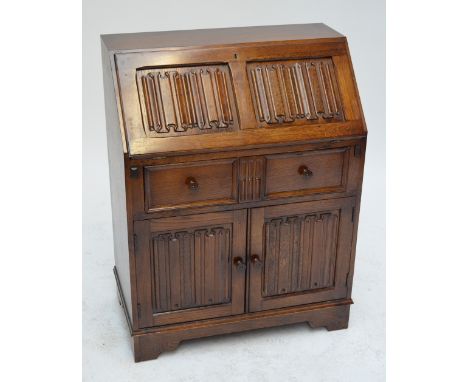 A reproduction oak fall front bureau with linen fold carving, the fall front enclosing sectioned interior above single drawer