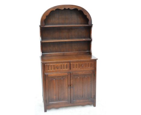 A reproduction oak dresser of two drawers including a cutlery drawer above two linen fold panel doors enclosing a shelf all b