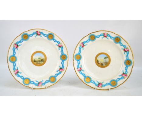 A pair of Minton porcelain shaped circular cabinet plates, each centred with a hand painted architectural and mountainous lan