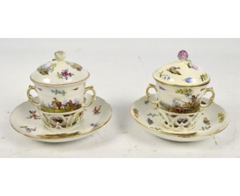 A near pair of 19th century Berlin porcelain hot water cups with covers and saucers, each painted with hunting scenes and flo
