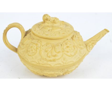 A 19th century Wedgwood cream basalt relief moulded teapot decorated with scrolling flowers and foliage, the cover with a dog