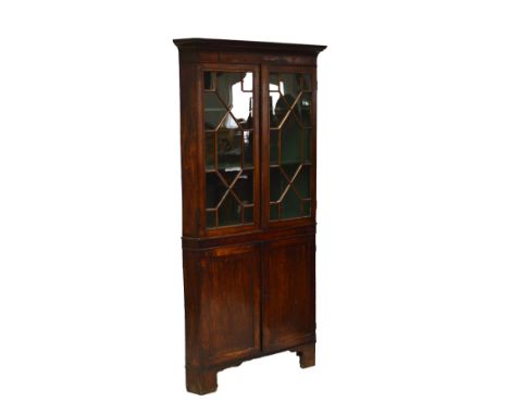 An early 19th century oak and mahogany crossbanded freestanding corner cupboard, the upper section with twin astragal glazed 