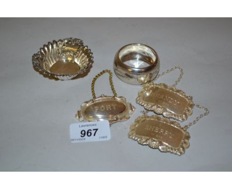 Three silver decanter labels, a napkin ring and a trinket dish