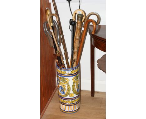 A cylindrical ceramic stick stand with Hispano-Moresque style decoration and a number of sticks including a cabbage stalk sti