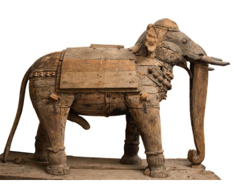 A large stripped wood Indian elephant:  dressed in ceremonial hangings, with drapes and bosses, having wood tusks and curled 