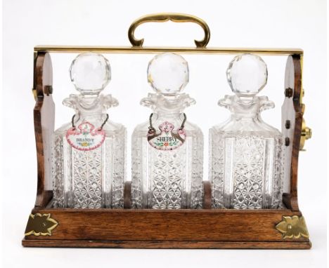 A Betjemanns Patent oak and brass mounted tantalus: containing three cut glass decanters and stoppers, with two enamel spirit