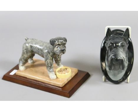 A Royal Doulton ceramic model of standard Schnauzer raised on a mahogany plinth along with a Scottish terrier wall mask.