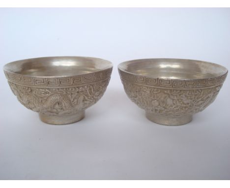 A pair of Chinese silvered porcelain bowls, decorated in raised relief with dragons chasing the flaming pearl, impressed Guan