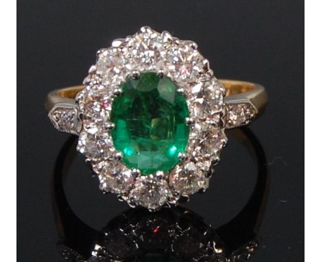 A ladies 18ct gold emerald and diamond cluster ring, the oval cut claw set emerald weighing approx 1.75ct, within a surround 