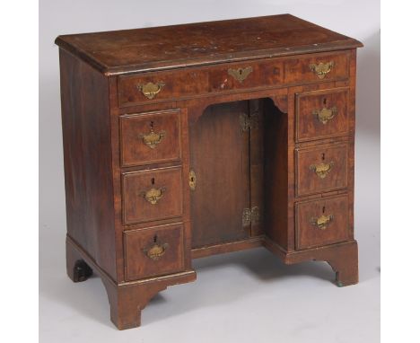 An early 18th century walnut and feather banded kneehole desk, having a four quarter veneered top with cross and feather band