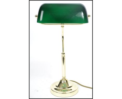A vintage 20th century bankers desk lamp having an adjustable green glass shade raised on a brass support and circular base. 