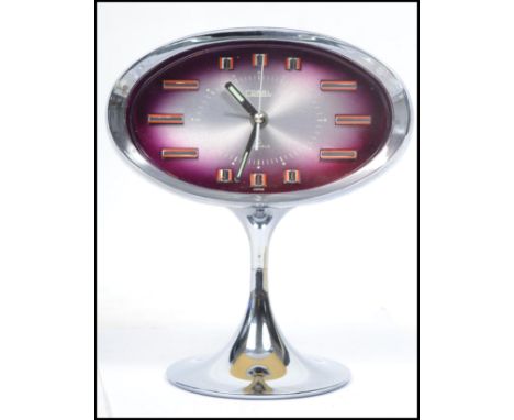 A vintage mid century Coral retro alarm clock of oval form having faceted hands and baton numerals raised on a tapering chrom