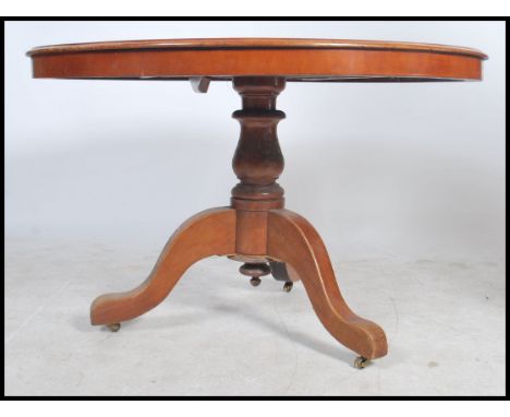 A large Victorian mahogany loo / tilt top dining table being raised on a tripod base with tapering column with circular tilt 