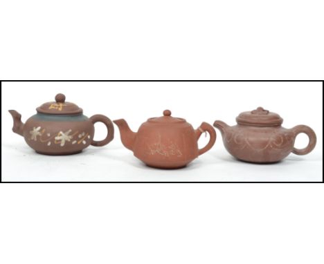 A collection of 3 Chinese terracotta yi-xing teapots. Each of varying design with scroll handles and spouts, each with lids. 