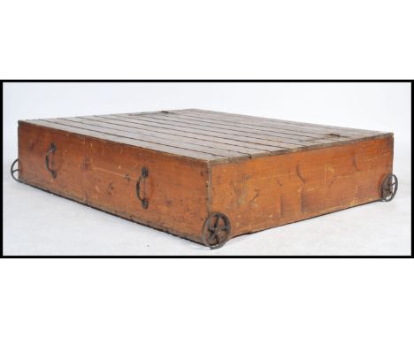 A vintage early 20th cenutry pine slatted storage bed box / coffee table raised on cast iron wheels having pull handles to tw