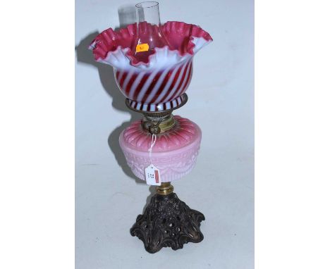 A Victorian oil lamp, having a frilled cranberry tinted vaseline glass shade above a pink glass font with raised Greek key an