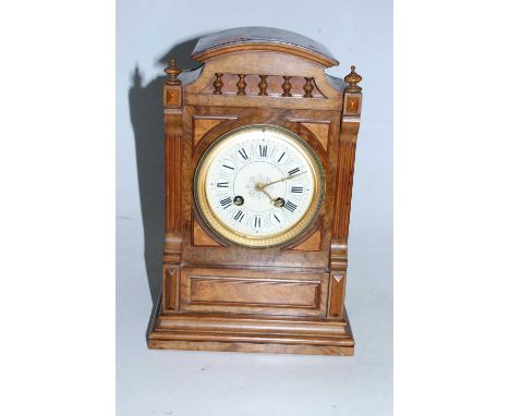 A late Victorian walnut cased mantel clock of architectural form having a circular dial with raised enamelled Roman numerals 