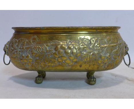 An oval brass planter, repousee embossed with grape vines, having lion head ring handles, on claw and ball feet, H.19 W.42 D.