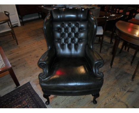 A green leather upholstered button wing back armchair on front cabriole supports, (81cm wide).