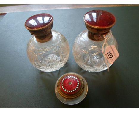 A pair of crystal cut glass scent bottles, each with silver and red enamel mounts, together with a glass dressing table jar w