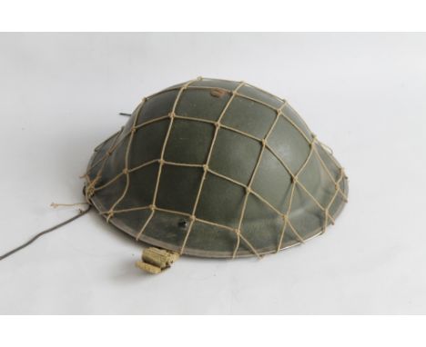 A BRITISH BRODIE TYPE HELMET with camouflage net, dated 1939 to chin strap anchor point
