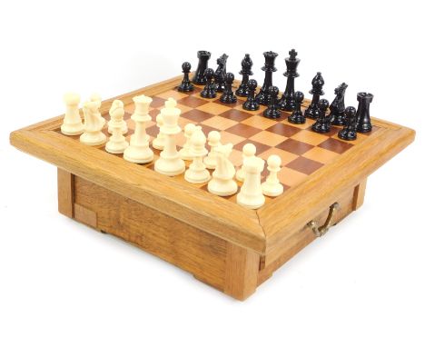 A teak chess board, with moulded top and two drawers for pieces, with high gloss chess pieces, the knight 10cm high.