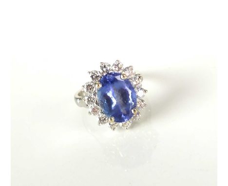 A tanzanite and diamond oval cluster ring, designed as a central oval mixed cut tanzanite claw set in white metal within a bo