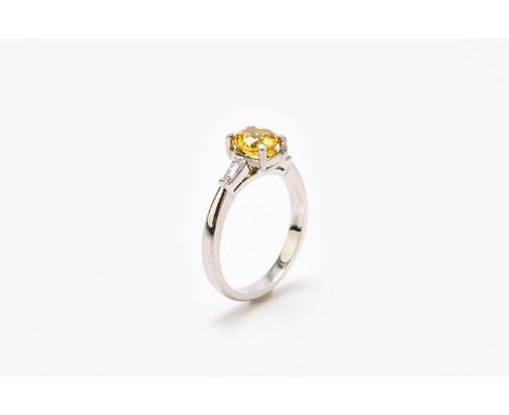 A platinum yellow zircon and diamond ring, designed as a central round mixed cut yellow zircon, claw set to tapering baguette