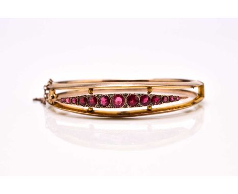 A 9ct gold graduated red paste set hinged bangle, the integral clasp with attached safety chain, presented within case, weigh