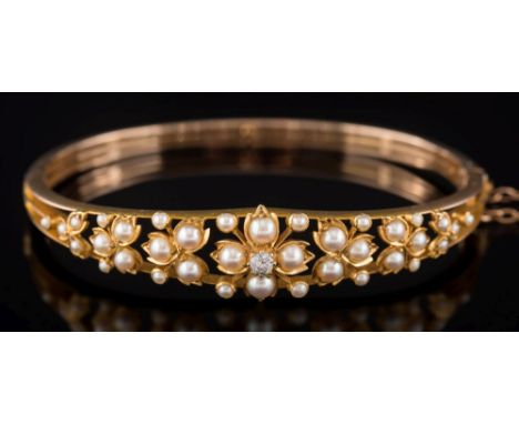 An Edwardian gold, diamond and seed pearl hinged bangle: with openwork foliate clusters of split seed-pearls and central old 