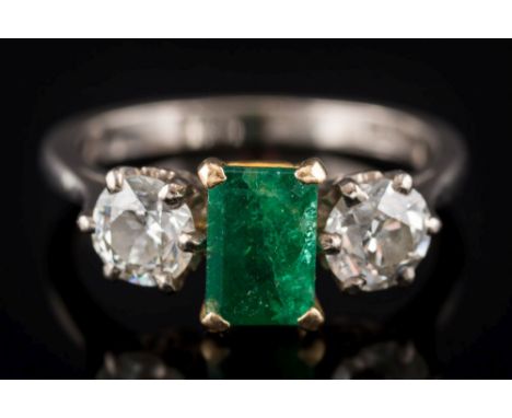 An emerald and diamond three-stone ring: the central rectangular emerald approximately 7.4mm long x 4.9mm wide and in four cl