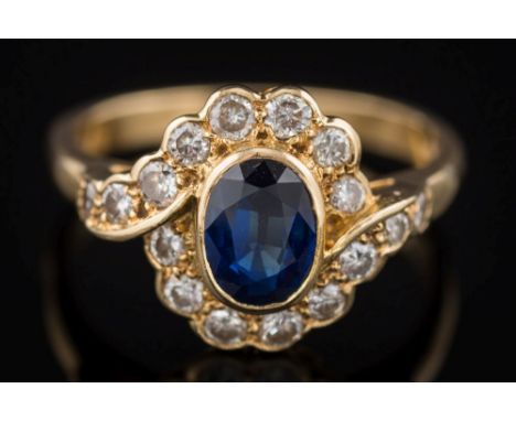 An 18ct gold, sapphire and diamond oval cluster ring: the central oval sapphire 7mm x 5mm, claw-set within a surround of bril